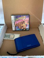 Blue Nintendo DS, three game cartridges in plastic case, and Slingo Quest game case inside a cardboard box.