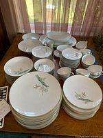 Overhead view showing a large set of white china with bamboo motif and gold trim, includes multiple stacks of plates, bowls, cups, and platters arranged on wooden table.