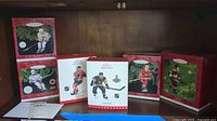Photo of six boxed Hallmark Keepsake hockey player ornaments on a wooden shelf, showing their collectible packaging with pine branch background and red boxes.