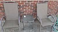 Front view of two patio chairs flanking a small glass top table against brick wall