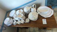 Overview of Pfaltzgraff Heritage white dinnerware set displayed on wooden surface including cups, bowls, platters, tureen, and pitcher.