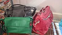 Overview of three handbags: green, gray and red on wire shelf.