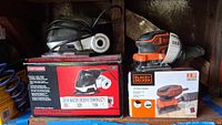 Craftsman Cyclone 4-in-1 Sander and Black and Decker 1/4 Sheet Sander in original boxes shown side by side on shelf.