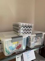 Three containers filled with sewing patterns, two white lidded with grey latches, one smaller zigzag black and white container on top.