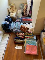 Overview of sewing materials including fabric bolts, remnants, cotton batting, elastic, ribbons, and plastic cutting mats arranged on the floor.