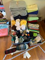 Stacked rolls of fleece and cotton fabric, assorted colors and patterns, with notions and ironing board visible.
