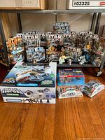 Photo showing most of the lot, unopened Star Wars Galactic Heroes figures and toy vehicles arranged on floor under shelf