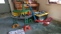Full view of Thomas the Tank Engine playset with elevated track, support pillars, bridge jump, and yellow tub containing track pieces and cars.