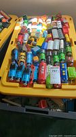 Photo showing a variety of Thomas the Tank Engine and Friends train engines, rail cars, and accessories laid out on a yellow plastic tub.