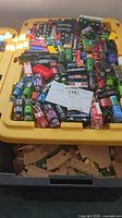 Yellow tub filled with numerous Thomas the Tank Engine wooden train cars and plastic storage tub lid.