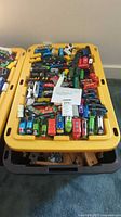 Top view of yellow storage tub filled with multiple Thomas the Tank Engine wooden train cars, coaches and tracks pieces.