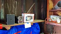 Shelf with two vintage box cameras, Garmin NuviCam LMT in box, and blue tarp underneath