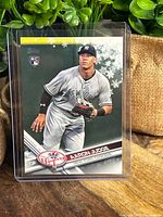 Front view of 2017 Topps Aaron Judge MVP Rookie Holiday Yankees baseball card in protective sleeve on wood surface with greenery background.
