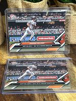 Two Jackson Holliday rookie baseball cards in protective cases showing him running after hitting his first MLB home run grand slam, with stadium background and card details visible.