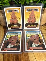 Four Garbage Pail Kids cards laid out front with two from 11a/b set and two from 14a/b set in clear protective cases.