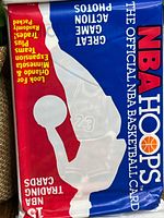 Front view of the sealed NBA Hoops basketball card pack showing official logos, colors, and Michael Jordan jersey visible behind the packaging.
