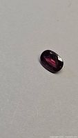 Oval faceted purple sapphire showing red tones and clarity on a white background.