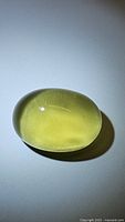 A close-up photo of a natural lemon citrine cabochon gemstone with an oval shape and smooth polished surface on a white background.