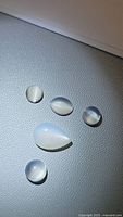 Five polished catseye moonstone gemstones showing translucent milky white color and distinct catseye effect on a textured grey surface.