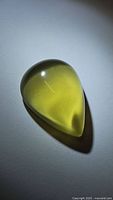 Pear-shaped cabochon lemon citrine gemstone showing deep yellow color and smooth polished surface against neutral background with shadow.
