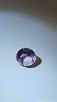 Round-cut natural amethyst stone showing pink-purple coloration and internal inclusions on a plain background.