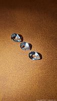 Three pear cut natural Brazilian aquamarine gemstones placed on a textured tan surface.
