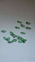 Photo of multiple natural marquis cut calibrated emerald gemstones spread out on a neutral background showing shape, size and color.