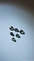 Photo showing six pear shaped green sapphires with blue undertones on a light background.
