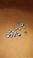 Top view of 14 loose round cut baby blue topaz gemstones scattered on a leather-like brown surface, showing their size, shape, and color.