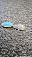 Two marquis cut faceted Ethiopian crystal opals on textured dark background showing iridescent colors.