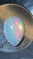 Close-up of pear-shaped Ethiopian opal cabochon showing bright play of colors under light.