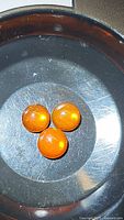 Three round orange fire opal cabochons arranged in a triangle on a dark circular surface showing color and internal reflections.