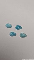 Four pear-shaped Larimar cabochons laid flat showing light blue and white marbled coloring.