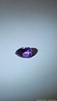 Close-up image of deep purple pear-shaped amethyst gemstone on a neutral background showing its color and cut.