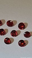 Photo showing nine round cut natural rubies with bright red color and orange undertones on a neutral background.