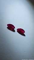 Photo of two marquis cut natural rubies on white surface with shadows, showing deep blood red color and clarity.
