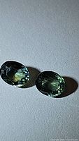 Two oval-shaped aqua blue-green sapphires side by side on a plain surface, showing color and facets.
