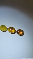 Photo showing three oval natural yellow sapphire cabochons varying in color from light yellow to deep amber, laying on a white surface.