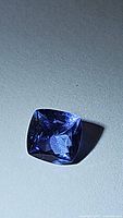 Cushion cut blue-purple tanzanite gemstone shown from the front under light, displaying facets and depth of color.