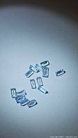 Multiple small natural baby blue topaz gemstones, baguette cut, spread on a light surface showing transparency and light blue color.