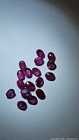 Multiple small oval cut rubies displayed on a plain surface under bright light showing their color and inclusions.