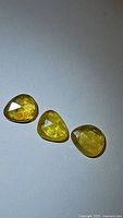 Three natural yellow sapphires placed on a white background showing their fancy rose cuts and inclusions under light.
