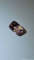 Close-up image of rectangular cushion-cut pink-peach-purple sapphire gemstone on plain background.