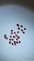 Top view of 27 round faceted hot pink sapphire gemstones on a white background showing deep red tones and diamond cut facets.