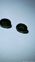 Photo shows two oval cut vivid green Tsavorite garnet gemstones on white background with visible facets and clarity.