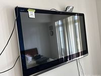 Front view of Sharp Aquos TV mounted on wall, showing reflective screen and part of room reflection.