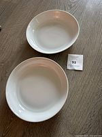 Two white round pasta bowls placed on a wood table, showing one inside and the other in front view.