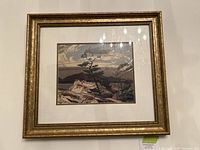 Framed landscape print hung on wall with gold decorative frame, white mat, and glass showing stylized trees and mountains.