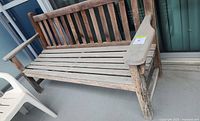 Front view of the weathered teak garden bench on a balcony with two armrests and a slatted seat and backrest.