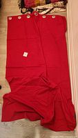 Two red blackout curtain panels spread out on the floor, showing metal grommets along the top for rod hanging.